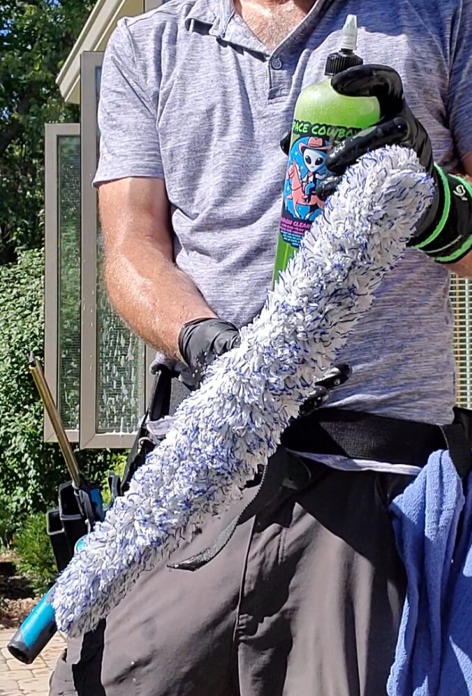 window cleaning technician standing by house applying soap to window scrubber