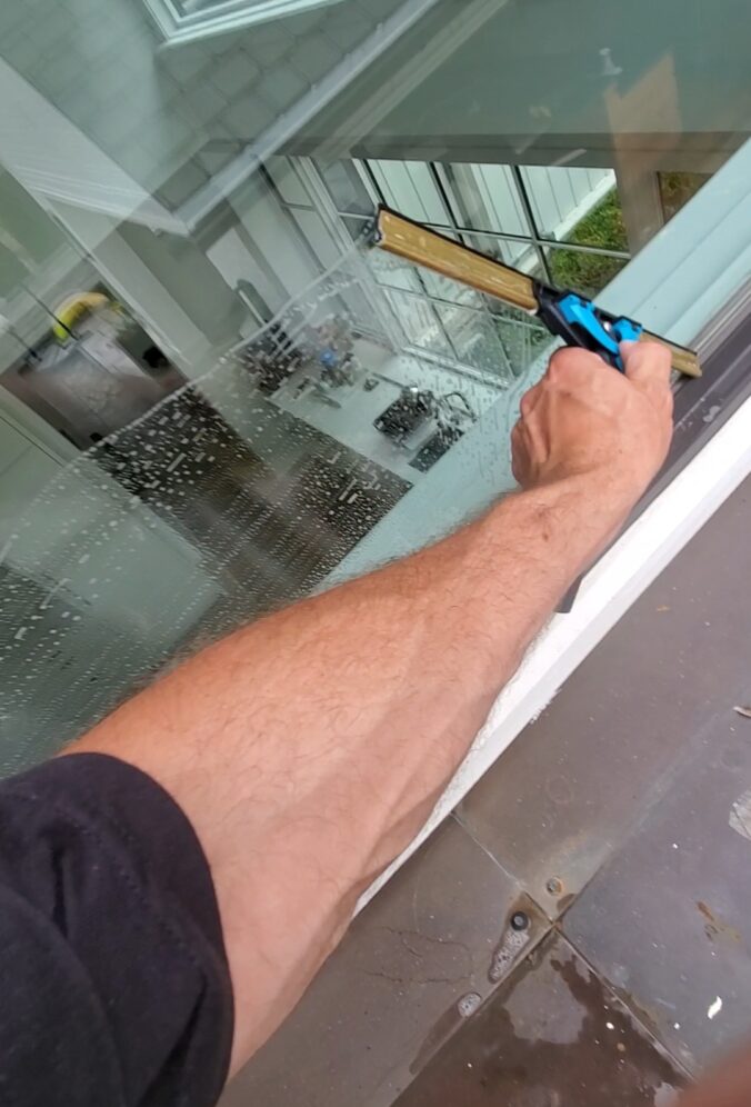 window cleaning technician arm squeegeeing a second story window