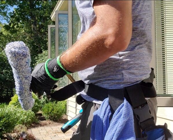 window cleaning technician standing next to house holding window scrubber